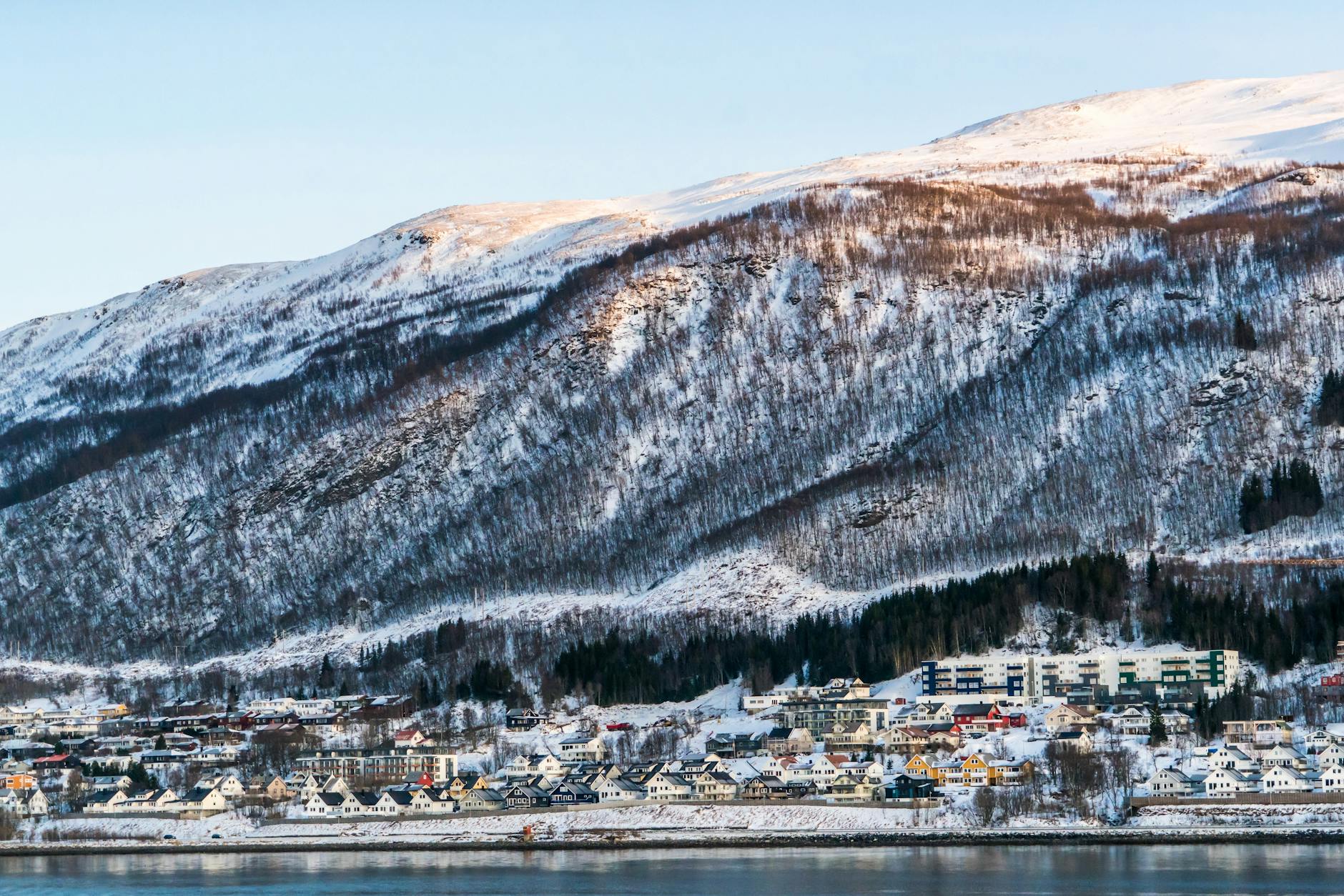 Norweskie miasteczko zimą nad fiordem u podnóża ośnieżonych gór