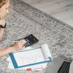 Kobieta na dywanie liczy budżet domowy na laptopie z kalkulatorem